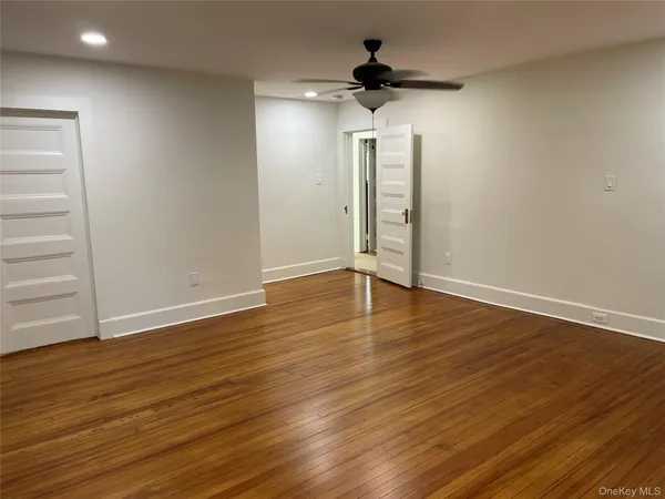a view of an empty room with wooden floor and a ceiling fan