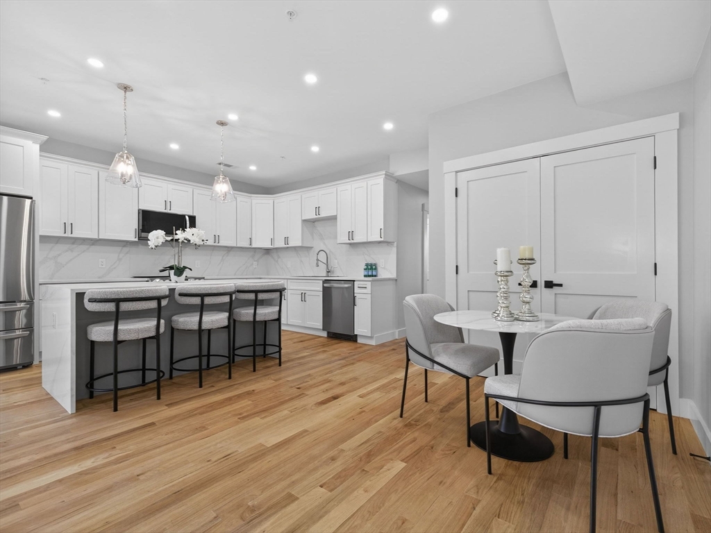 a kitchen with kitchen island stainless steel appliances a dining table chairs sink and cabinets