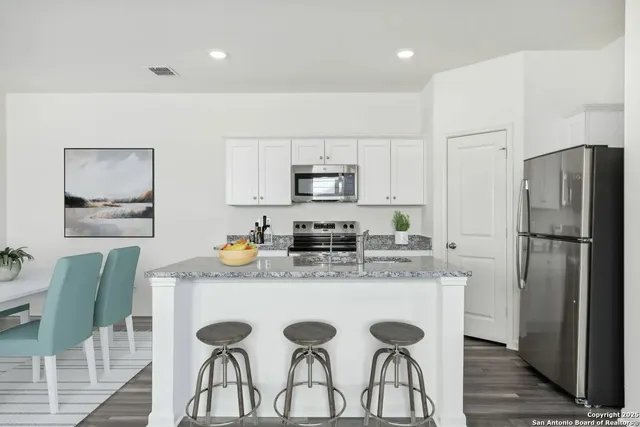 a kitchen with stainless steel appliances granite countertop a table chairs stove and refrigerator