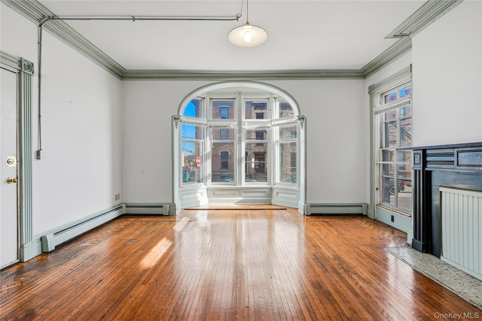 203 Grand Street, Unit 1 Newburgh, NY 12550 - Photo 1 of 10 Unfurnished living room with crown molding, hardwood / wood-style floors, a baseboard heating unit, and a decorative wall