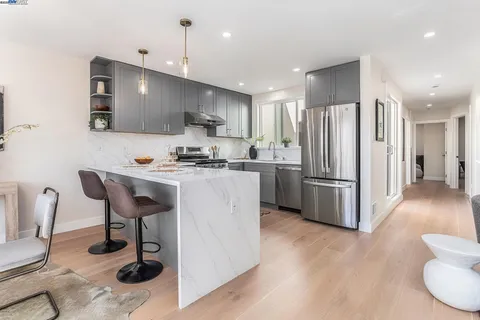 a kitchen with stainless steel appliances a refrigerator a stove a sink a dining table and chairs with wooden floor