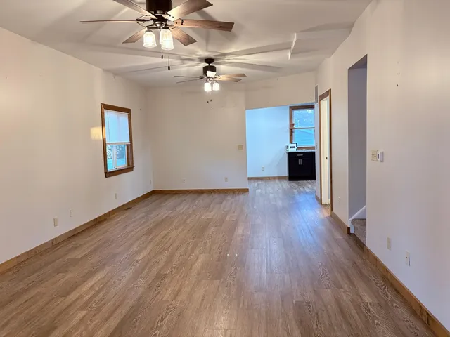 an empty room with wooden floor chandelier fan and windows