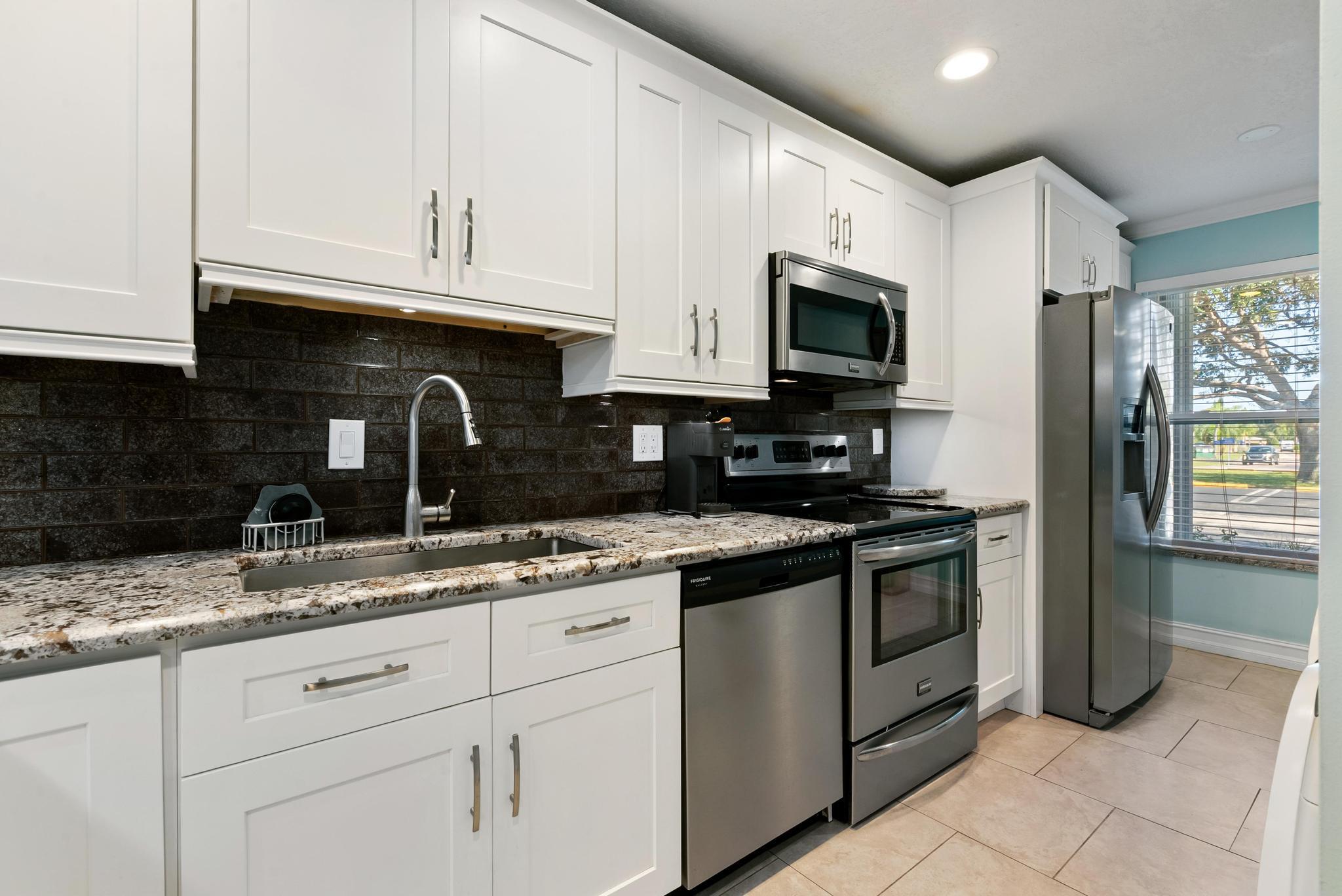 1280 Northwest 20th Avenue, Unit 101 Delray Beach, FL 33445 - Photo 8 of 31 a kitchen with granite countertop a sink stainless steel appliances and white cabinets