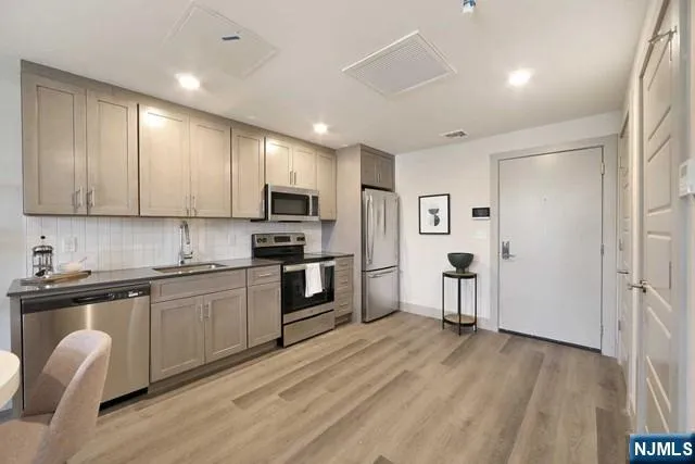 a kitchen with granite countertop a refrigerator a sink dishwasher a stove and white cabinets with wooden floor