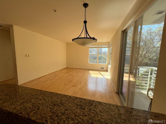 a view of a hallway to an empty room with wooden floor and a window