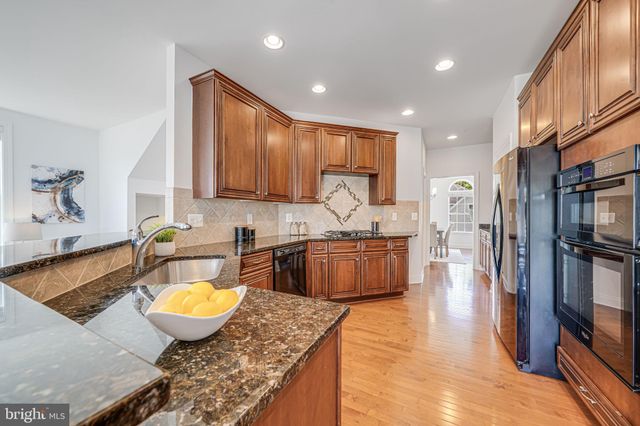 a kitchen with stainless steel appliances granite countertop a stove top oven a sink a dining table and chairs with wooden floor