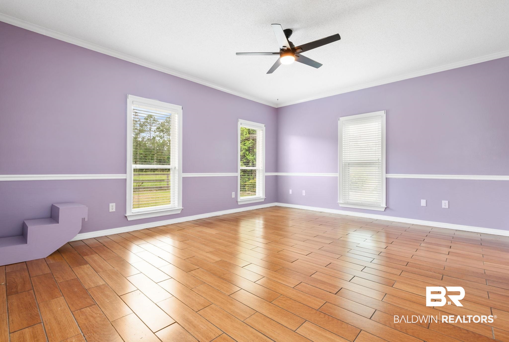 7540 2 Mile Road Irvington, AL 36544 - Photo 52 of 82 Spacious room featuring wood-finish flooring, three windows with blinds, a ceiling fan, crown molding, and wainscoting