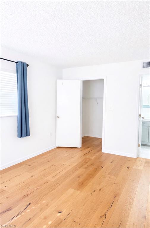 3325 Airport Road North, Unit F1 Naples, FL 34105 - Photo 7 of 7 Unfurnished bedroom with a textured ceiling, light wood-style floors, a walk in closet, ensuite bath, and multiple windows