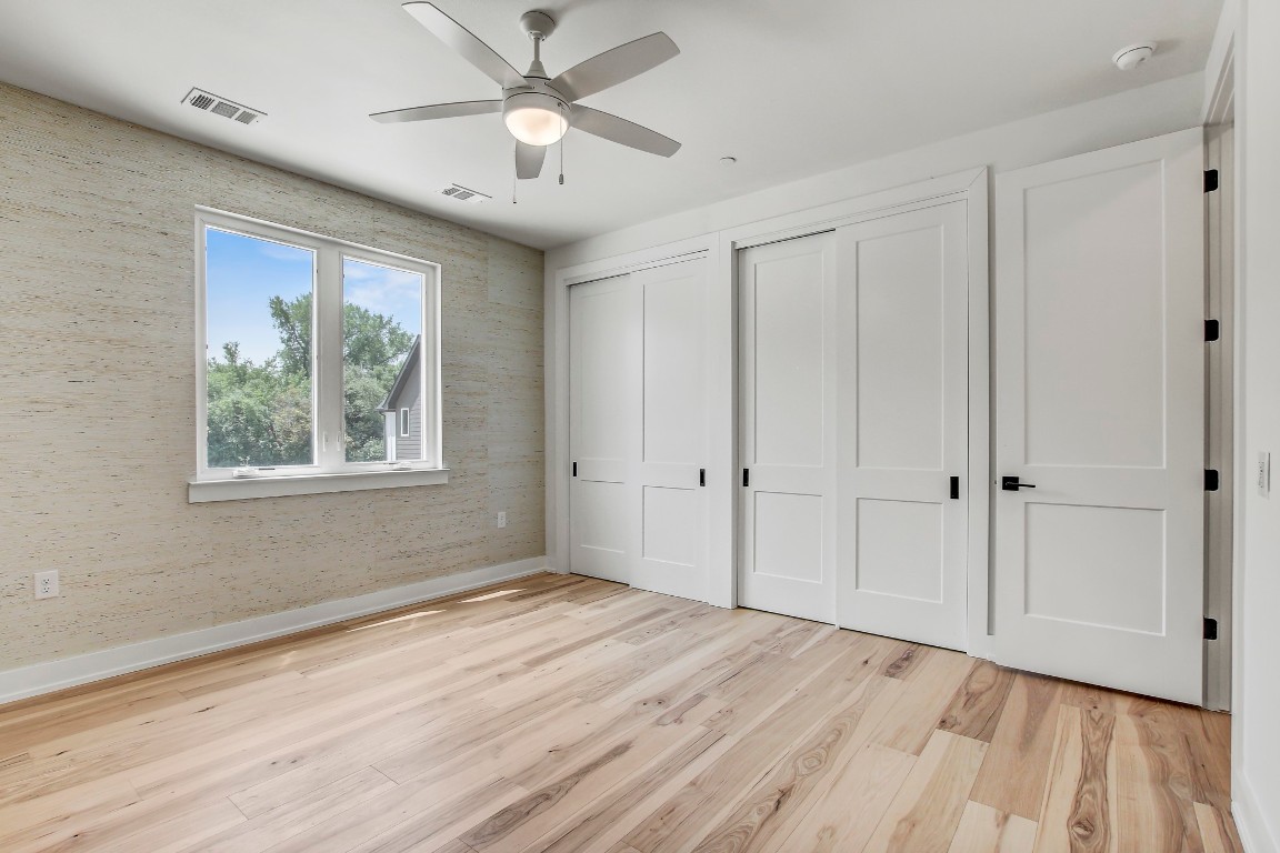 4127 East 12th Street, Unit 4 Austin, TX 78721 - Photo 14 of 32 Unfurnished bedroom featuring two closets, light wood-style floors, baseboards, ceiling fan, and wallpapered walls
