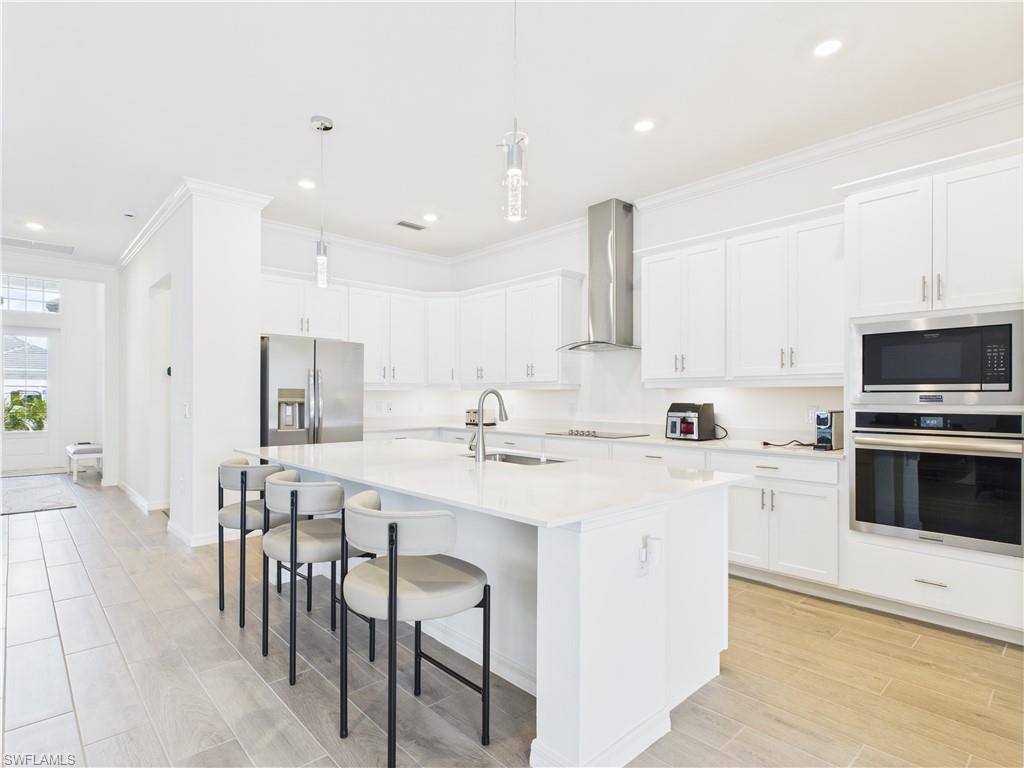 5412 Fancourt Links Way Ave Maria, FL 34142 - Photo 6 of 39 Kitchen featuring stainless steel appliances, crown molding, a kitchen breakfast bar, hanging light fixtures, and white cabinets