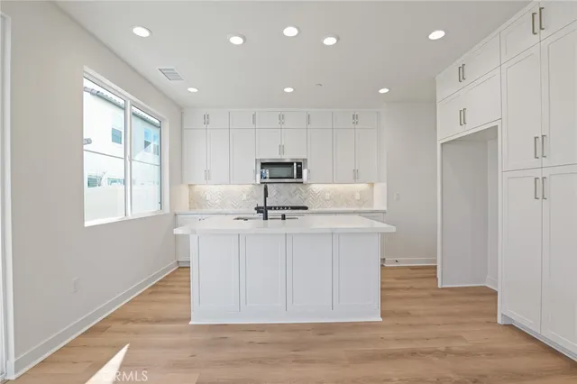 a kitchen with stainless steel appliances granite countertop a sink a microwave a refrigerator and white cabinets with wooden floor