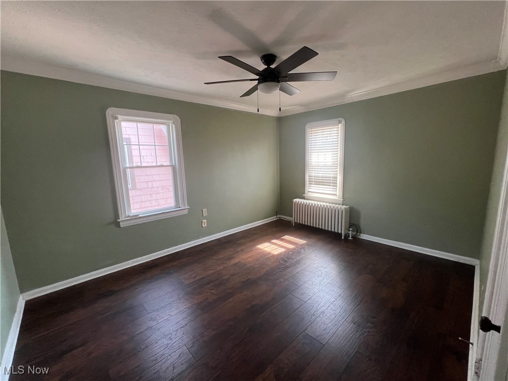 3505 Silsby Road Cleveland, OH 44118 - Photo 28 of 34 Unfurnished room with radiator, crown molding, dark wood-style flooring, baseboards, and a ceiling fan