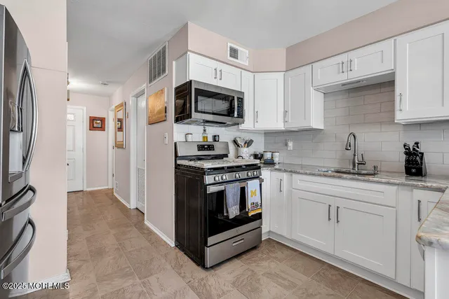 a kitchen with stainless steel appliances granite countertop white cabinets a sink a stove a refrigerator and a microwave