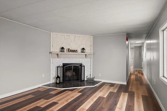 a view of an empty room with wooden floor fireplace and a window
