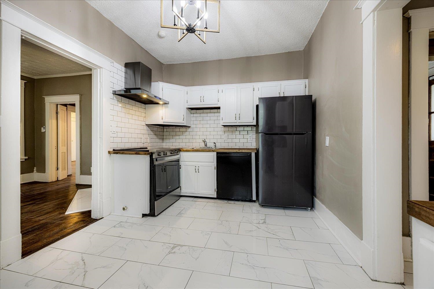 431 Alexander Street Memphis, TN 38111 - Photo 4 of 13 Kitchen featuring black appliances, a textured ceiling, wall chimney range hood, white cabinets, and backsplash
