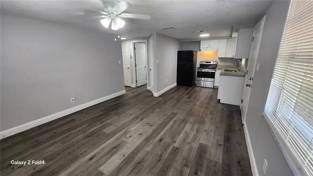 a view of an empty room with wooden floor a kitchen space with a sink