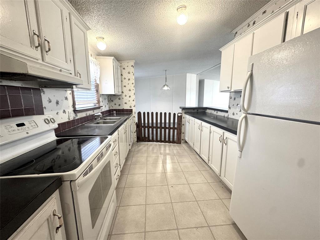 211 West F Street Munday, TX 76371 - Photo 10 of 27 a kitchen with granite countertop a refrigerator a sink a stove and white cabinets