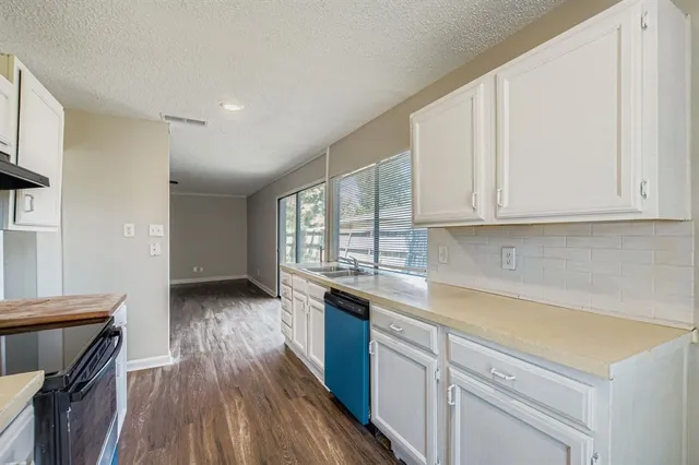 a kitchen with granite countertop a stove a sink and white cabinets with wooden floor