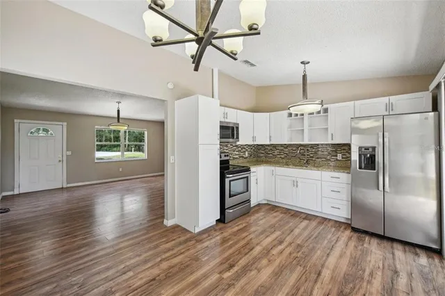 a large kitchen with cabinets wooden floor stainless steel appliances and a chandelier