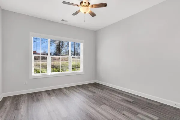 an empty room with wooden floor chandelier fan and windows