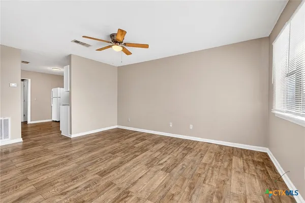 an empty room with wooden floor ceiling fan and windows