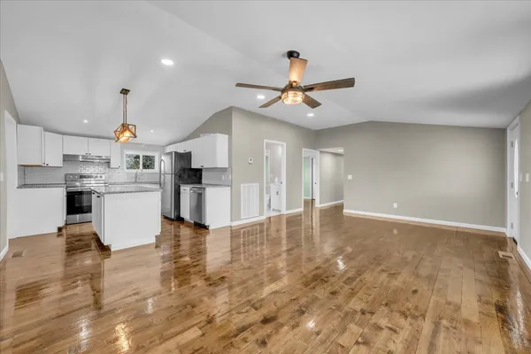 a view of a kitchen with kitchen island stainless steel appliances refrigerator stove and wooden floor