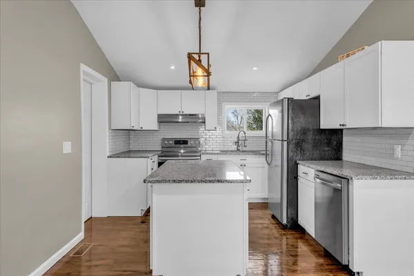 a kitchen with kitchen island granite countertop a stove a sink dishwasher a refrigerator and white cabinets with wooden floor