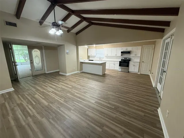 an empty room with wooden floor windows and kitchen view