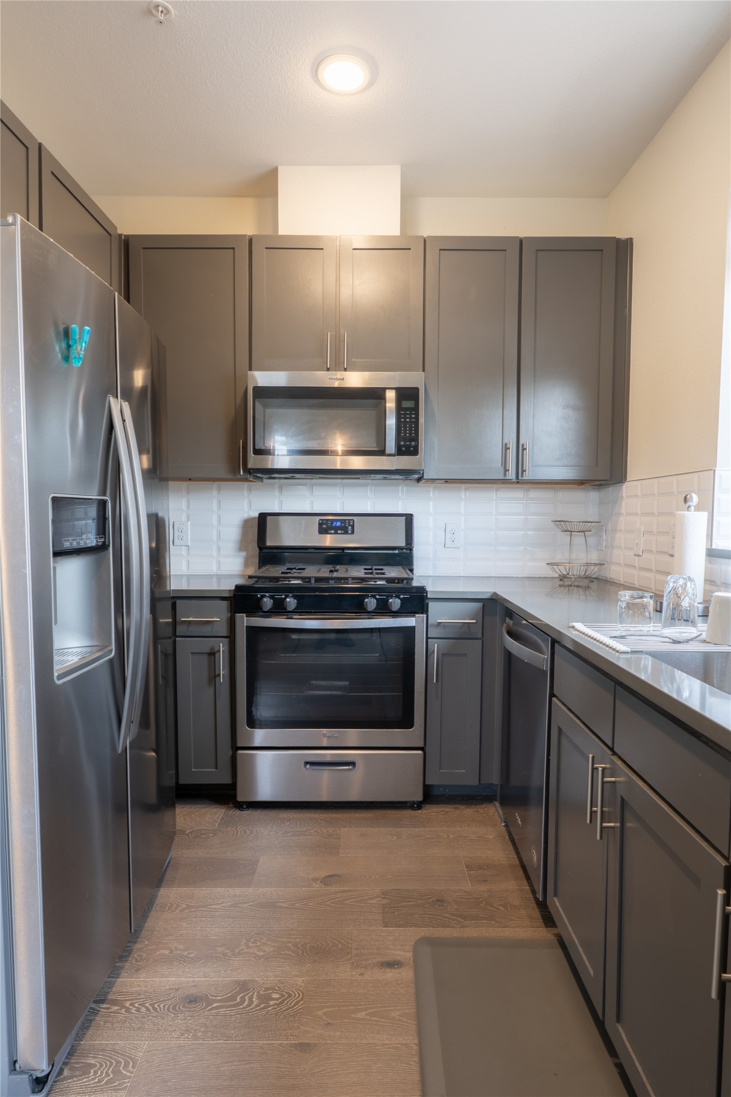 2827 Manor Road, Unit 4101 Austin, TX 78722 - Photo 14 of 38 The kitchen features stainless steel appliances, grey cabinetry, a light-colored subway tile backsplash, and light wood-style flooring