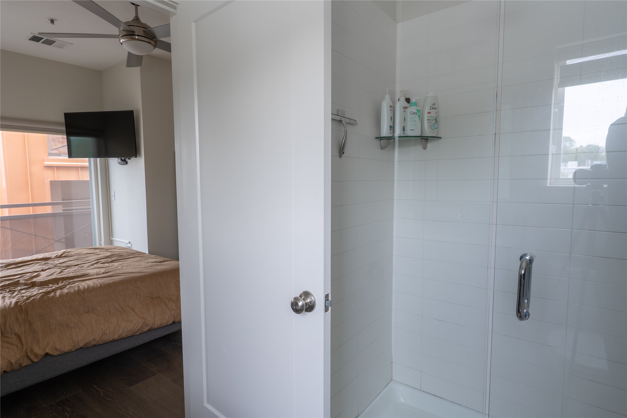 2827 Manor Road, Unit 4101 Austin, TX 78722 - Photo 22 of 38 The property features a shower with white tiled walls and a glass enclosure, alongside a room with dark flooring, a large window, and a ceiling fan