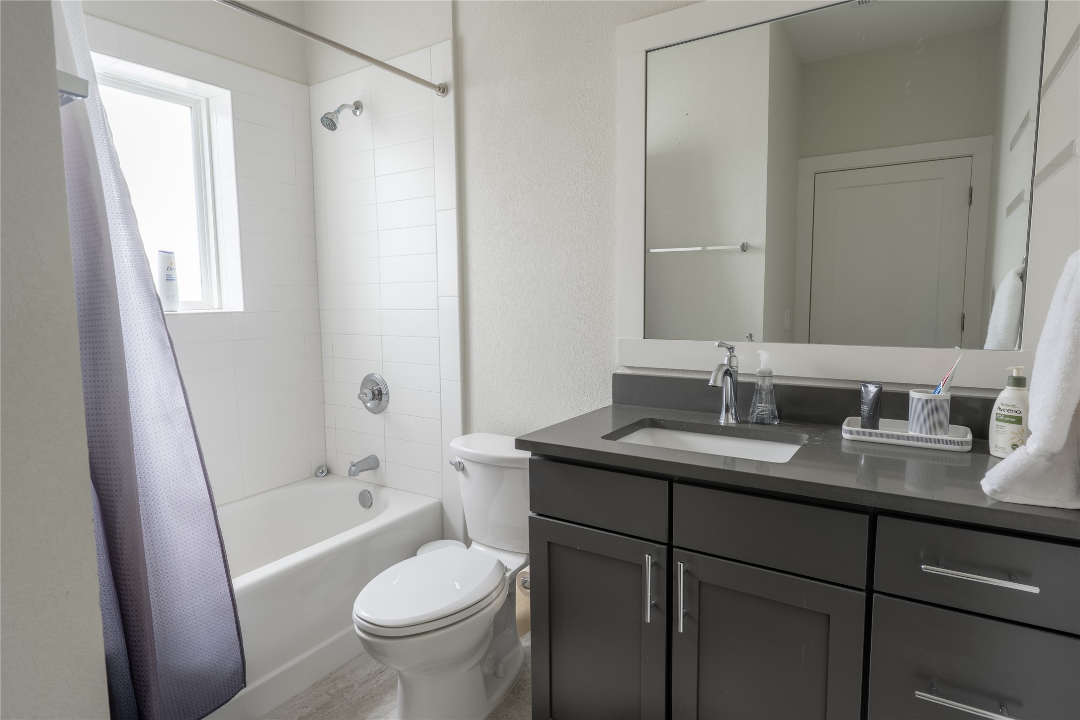 2827 Manor Road, Unit 4101 Austin, TX 78722 - Photo 32 of 38 Well-appointed bathroom featuring a tub and shower combination with subway tile surround, a window providing natural light, and a vanity with a rectangular sink and dark cabinetry