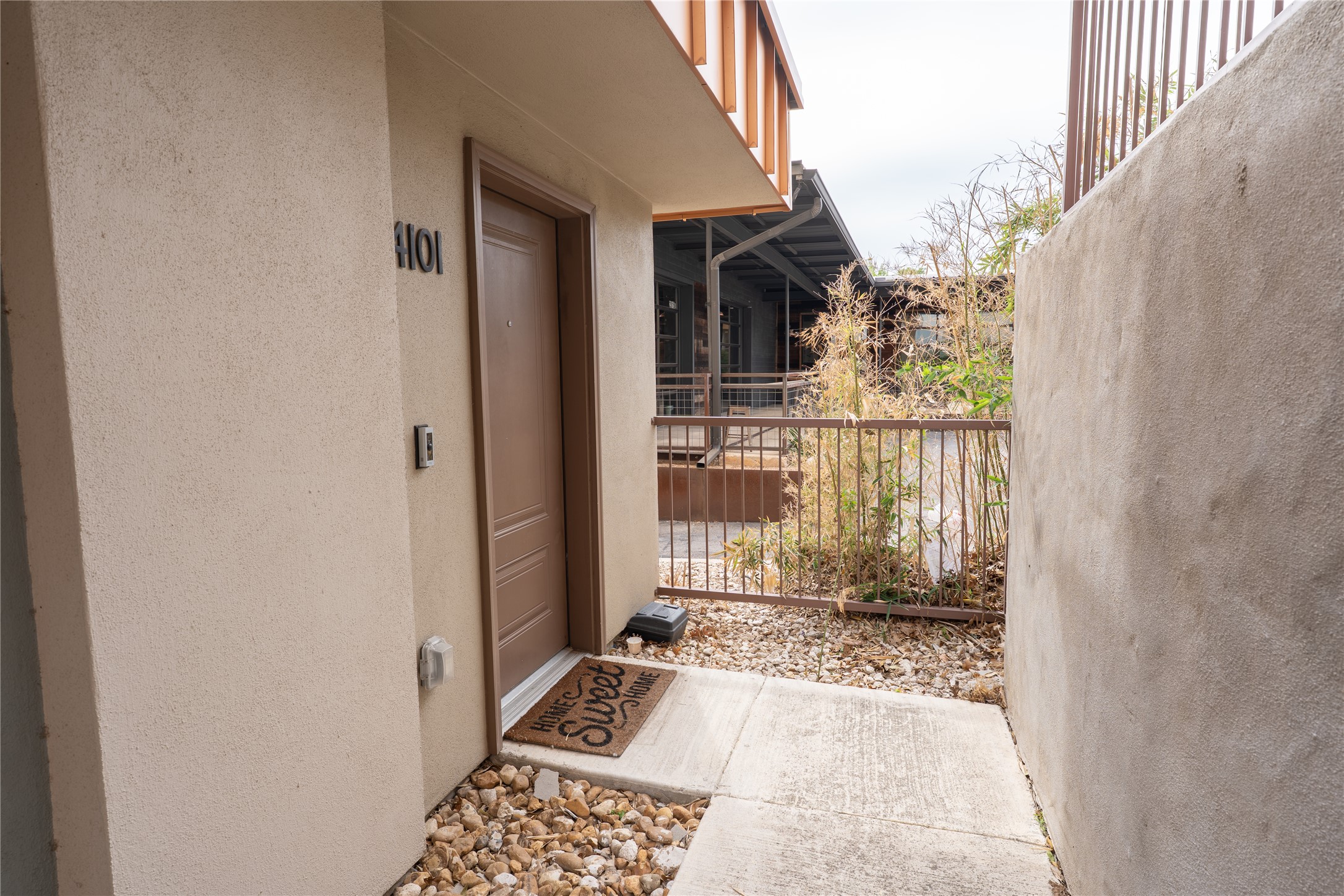 2827 Manor Road, Unit 4101 Austin, TX 78722 - Photo 35 of 38 The property features a brown entry door, a neutral-toned exterior wall, and a concrete pathway leading to the entrance