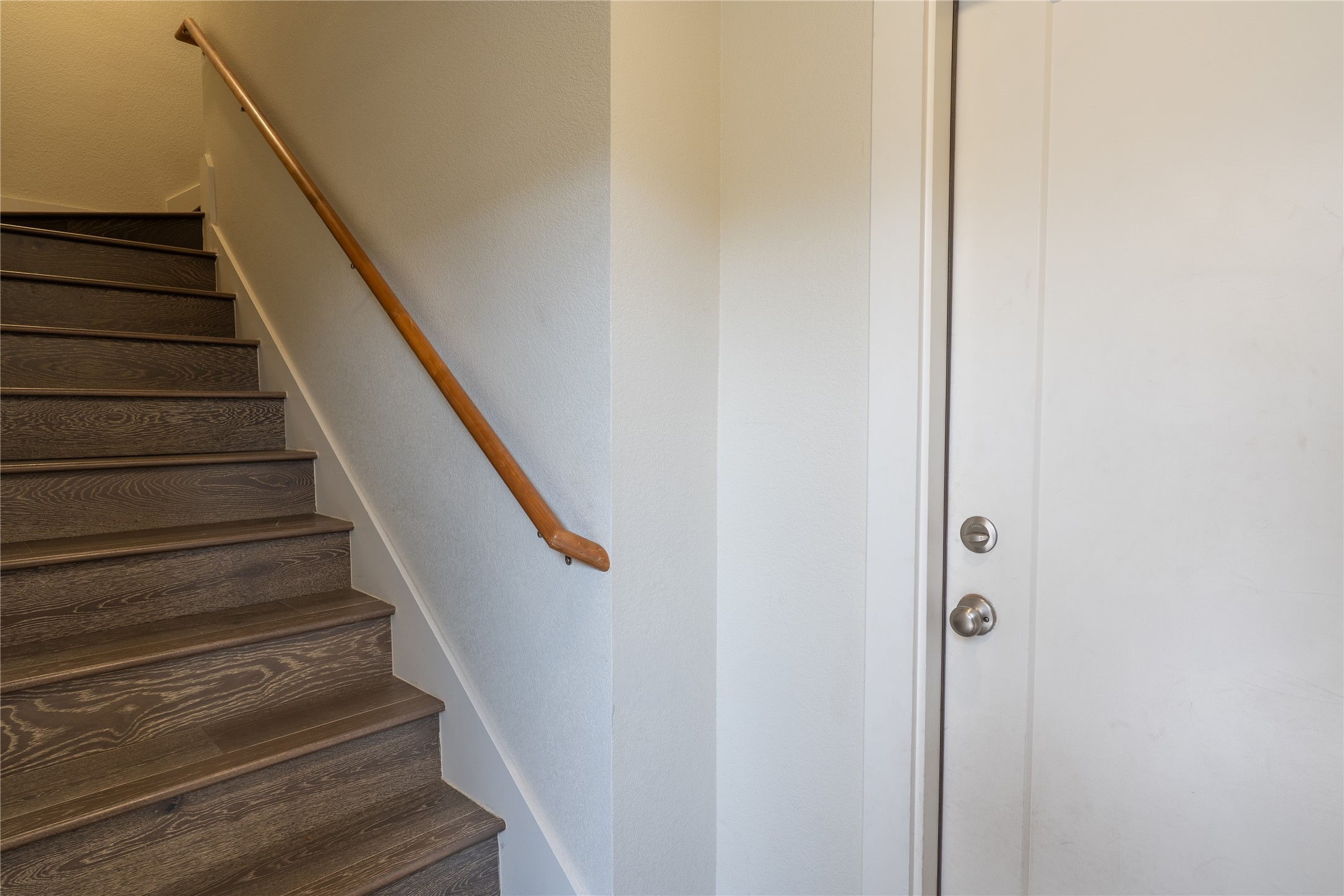 2827 Manor Road, Unit 4101 Austin, TX 78722 - Photo 36 of 38 The property features a staircase with dark wood treads and a light wood handrail, alongside a white entryway door with silver hardware