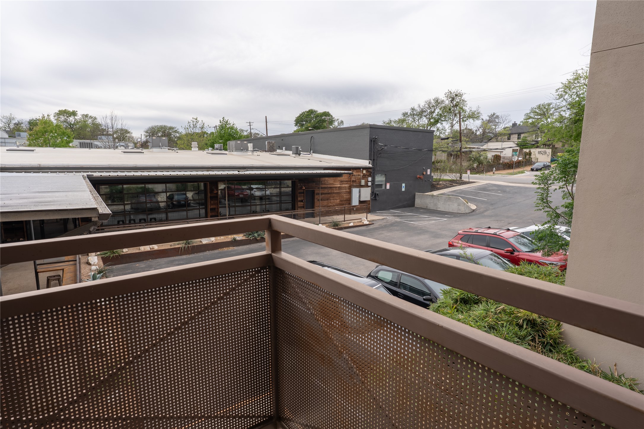 2827 Manor Road, Unit 4101 Austin, TX 78722 - Photo 9 of 38 The property features a balcony with a perforated metal railing, overlooking a paved parking area and buildings with flat roofs