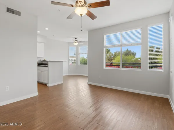 an empty room with wooden floor chandelier fan and windows