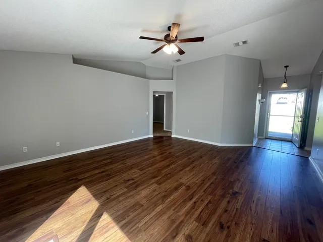 a view of an empty room with wooden floor and a ceiling fan