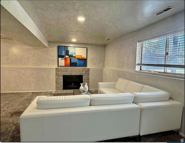 169 East 100 North, Unit B Logan, UT 84321 - Photo 2 of 11 Living room featuring a tiled fireplace with a dark insert, a large window with natural light, recessed ceiling lighting, and a visible ceiling beam