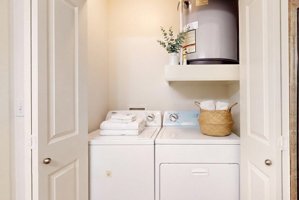 1010 Rosine Street, Unit 29 Houston, TX 77019 - Photo 14 of 16 This photo shows a compact laundry closet with a washer and dryer, neatly tucked between two doors. It includes shelving above for storage, holding a water heater and a basket with towels, adding functionality and convenience to the home. (Virtual Staging)