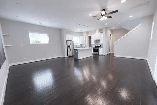 a view of an empty room with wooden floor and a kitchen