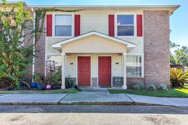 a view of a brick house with large windows plants and large tree