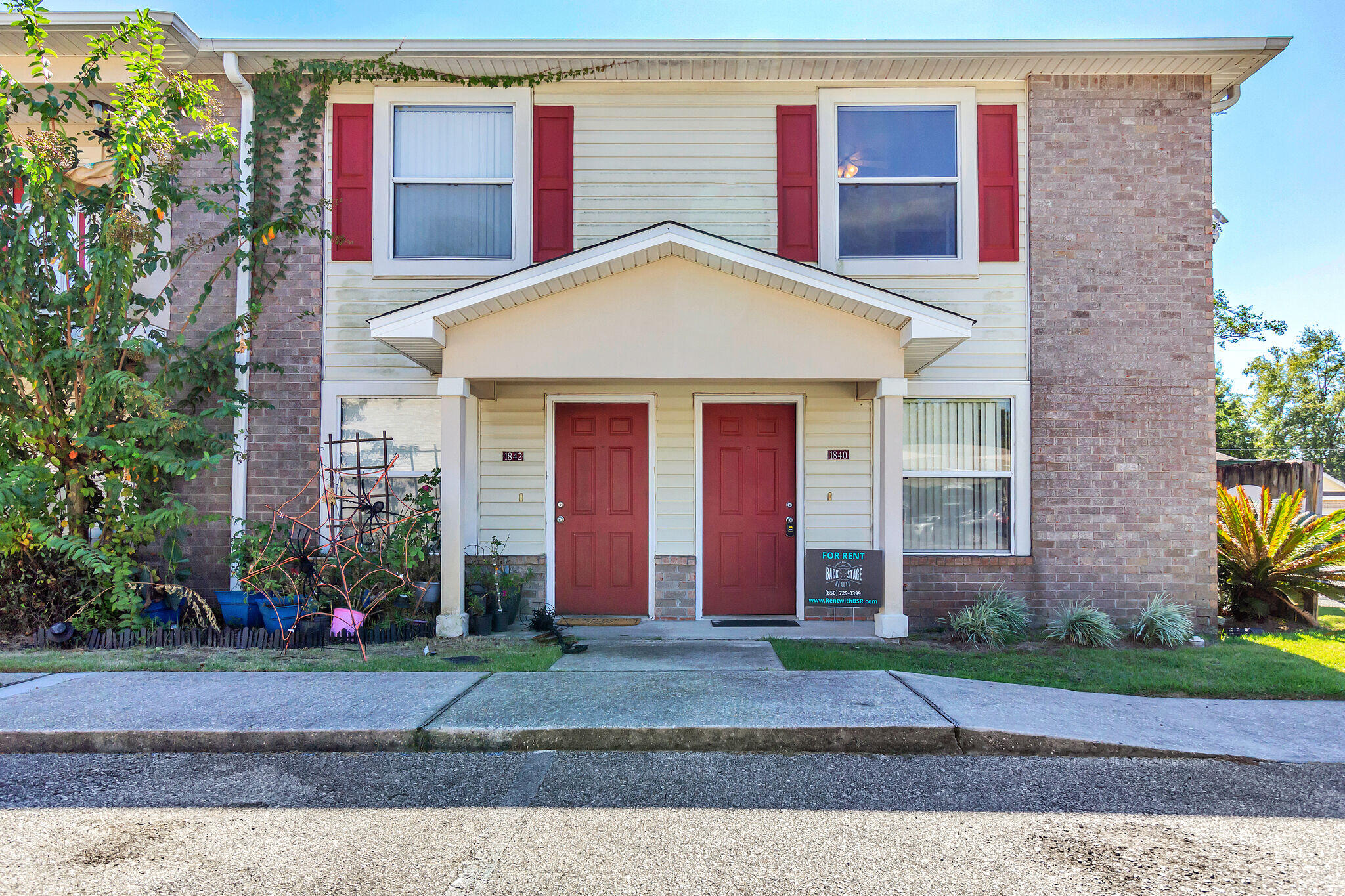 a view of a brick house with large windows plants and large tree