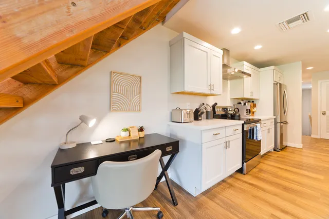 a kitchen with stainless steel appliances kitchen island granite countertop a sink a stove a refrigerator and white cabinets with wooden floor