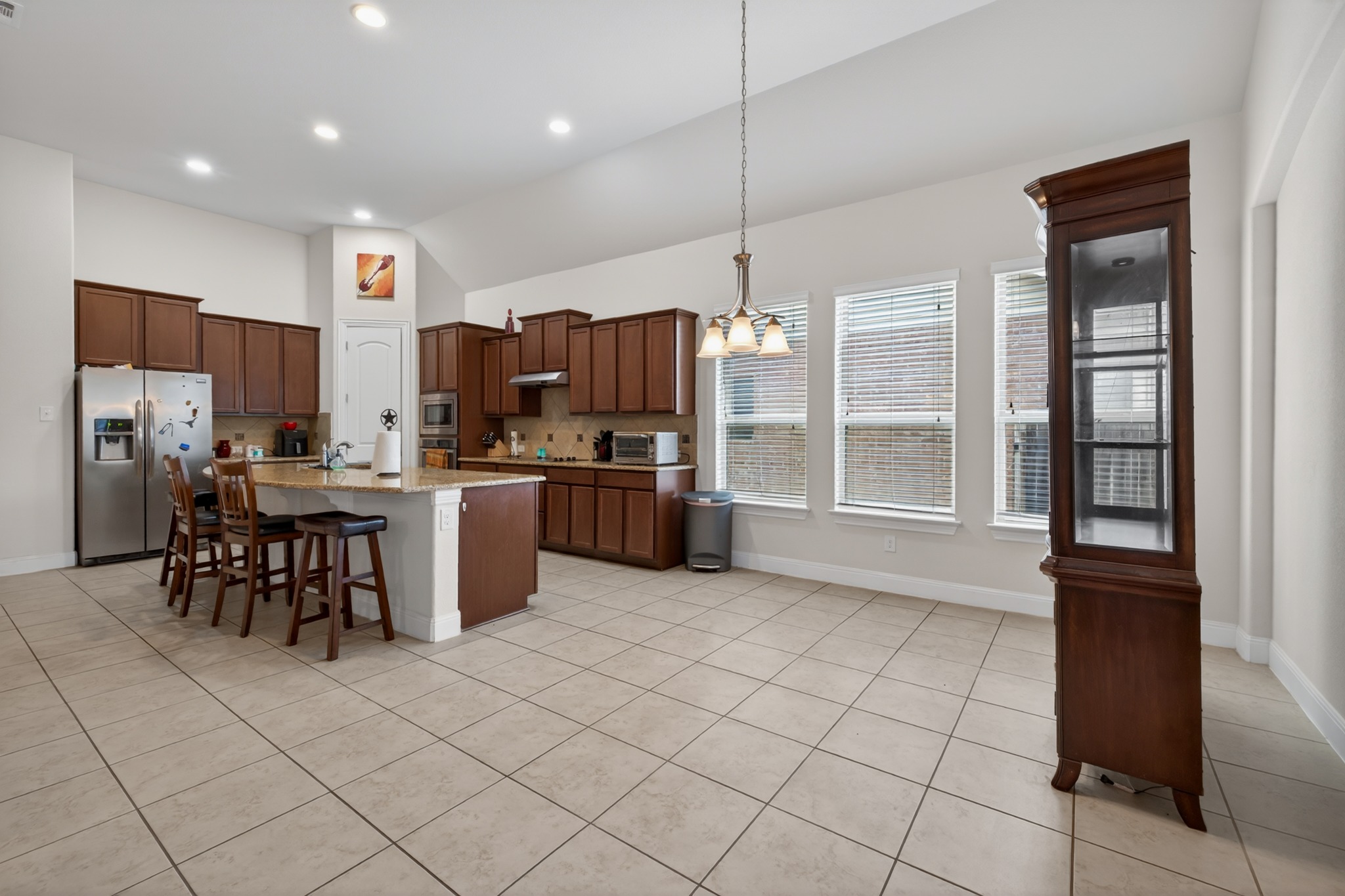 1017 Tabernash Leander, TX 78641 - Photo 10 of 38 Spacious kitchen and dining area featuring an expansive island, abundant dark wood cabinetry, stainless steel appliances, and light-toned tile flooring