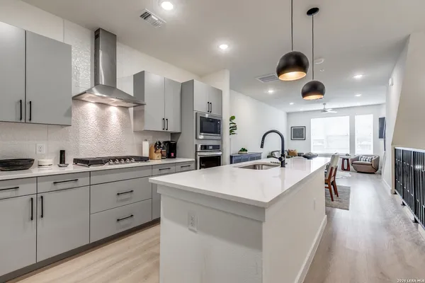 a large kitchen with stainless steel appliances a stove a sink a oven and a dining table with wooden floor