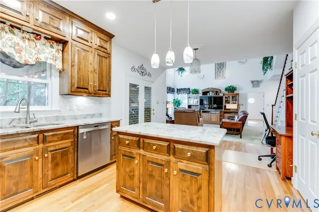 a kitchen with stainless steel appliances granite countertop a sink dishwasher and a flat tv screen next to a large window with wooden floor