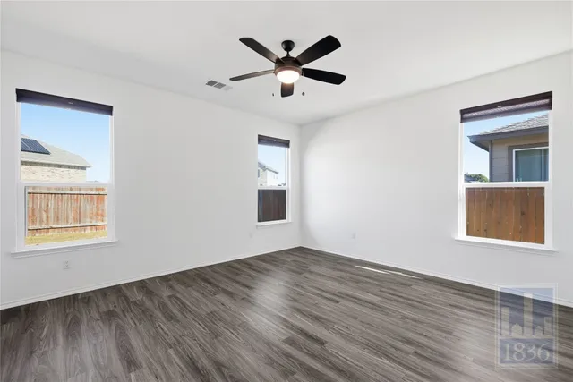 a view of an empty room with wooden floor and a ceiling fan