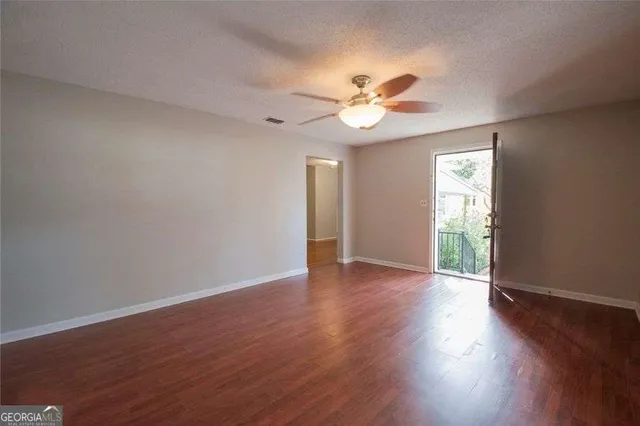 an empty room with wooden floor chandelier fan and windows