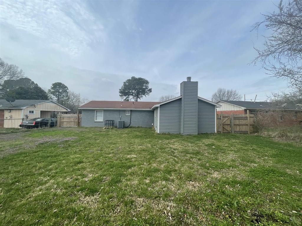 3998 Leech Road Memphis, TN 38109 - Photo 3 of 5 Expansive green space featuring a wood fence, a single-story residence with a gray exterior, and a prominent chimney