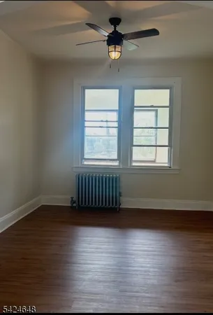 an empty room with wooden floor chandelier fan and windows