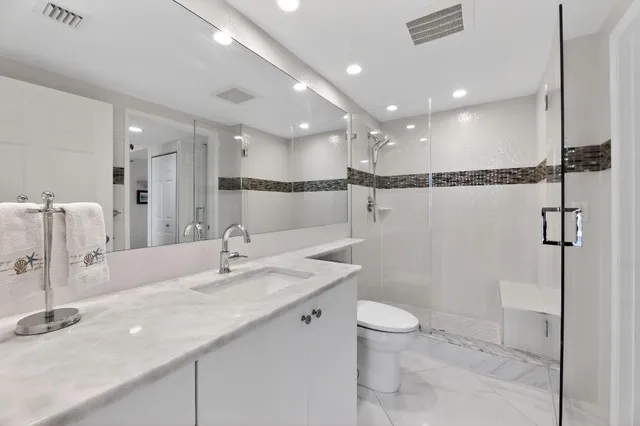 a bathroom with a granite countertop sink a toilet a large mirror and shower